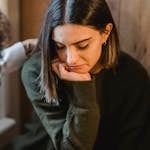 Crop woman tapping shoulder and comforting upset female friend while sitting at home together